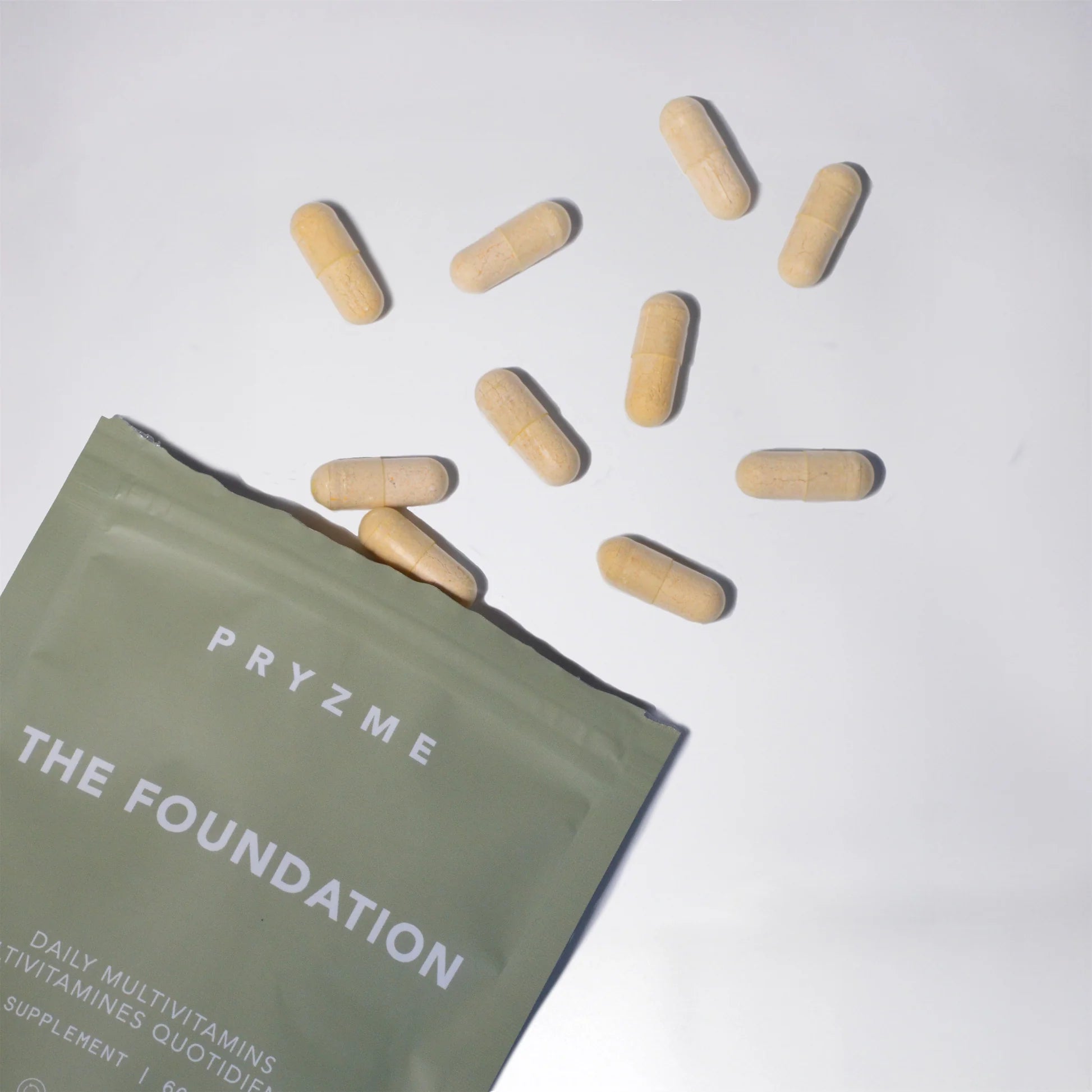 Pryzme The Foundation daily multivitamins packaging with scattered capsules on a light background